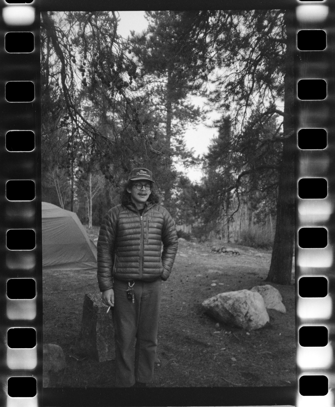 Judah standing at a campsite among tall pines, black and white film