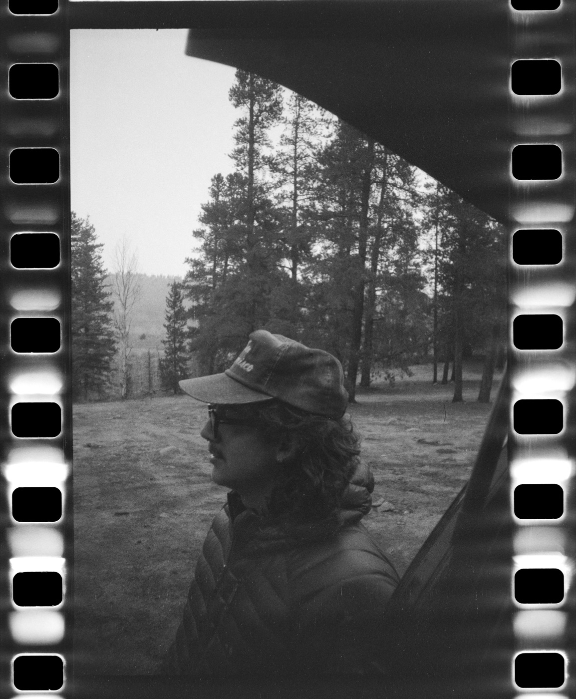 Judah in profile wearing a cap, pine trees behind, black and white 35mm film